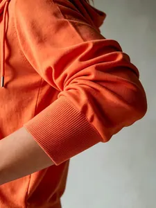 Dettaglio del cardigan in maglia arancione con cappuccio, polsino a coste e trama
