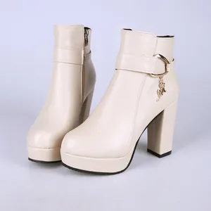 Détail de bottines à plateforme beiges avec talon épais et breloque dorée en lettre M