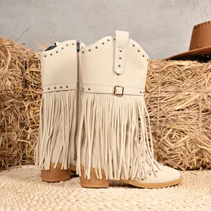 Cream western mid-calf boots with fringe, rivets and buckle on rustic hay background