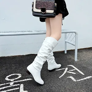 Detailed close-up of elegant white mid-calf slouch boots with low block heel in street setting