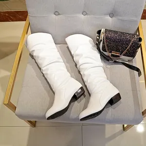 White slouchy mid-calf leather boots with chunky wooden heels presented on a chair.