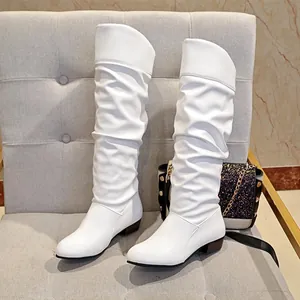 Detailed side view of elegant white slouchy knee-high boots on a gray tufted chair