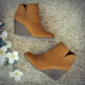 Seitenansicht brauner Wildleder-Keilstiefeletten auf strukturiertem Boden mit Blumen