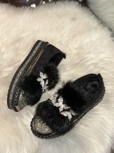 Close-up of black platform loafers featuring plush fur trim and rhinestone butterfly detail