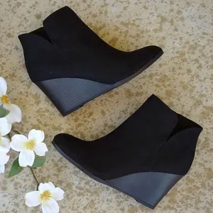Nahaufnahme von schwarzen Keilstiefeletten mit elegantem V-Ausschnitt auf Fliesen