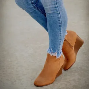 Detaillierte Makroansicht stylischer brauner Keilstiefeletten aus Wildleder mit Jeans mit Fransen