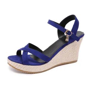 Close-up of blue suede crossover strap wedge sandals featuring gold buckle charm