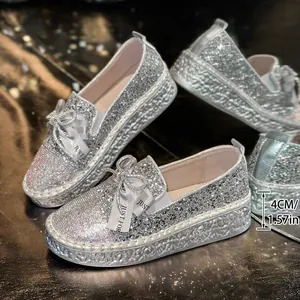 Detailed view of silver glitter loafers with rhinestone bows and 4cm platform.