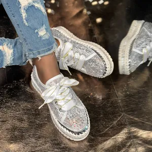 Close-up detail of silver rhinestone sneakers with white satin laces on metallic floor