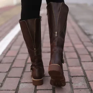 Detailed back view of brown high-top knight boots with functional zippers on brick pavement
