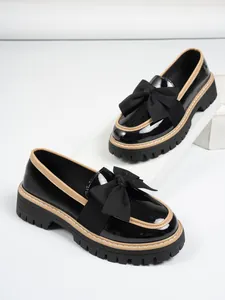 Close-up of stylish black patent leather loafers with a bow and thick platform sole