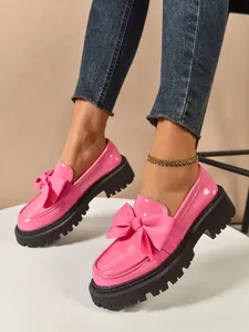 Close-up of pink patent leather loafers featuring a large bow and thick lug soles