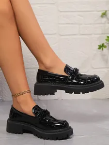 Gros plan de mocassins noirs à texture crocodile avec semelles compensées.