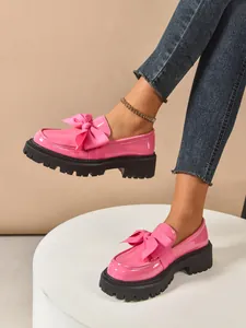 Detail shot of pink patent leather bow loafers with chunky platform sole and jeans.