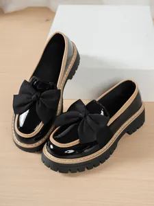 Close-up of black patent leather loafers with a large bow and chunky platform sole