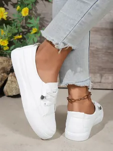 Detailed view of women's white casual sneakers worn with frayed denim jeans outdoors
