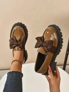 Detail view of brown patent leather platform loafers with oversized fabric bow.