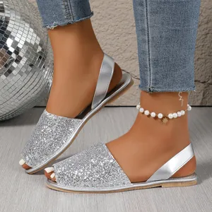 Close-up of sparkling silver glitter peep-toe flat sandals worn with a stylish pearl anklet