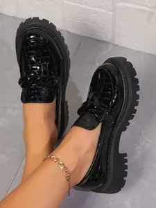 Gros plan sur des mocassins noirs motif crocodile avec semelle compensée et chaîne