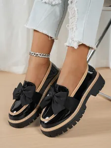 Detail view of stylish black patent leather loafers with large bow and thick lug sole.