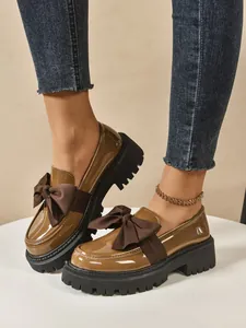 Detailed view of stylish brown patent leather bow loafers with thick platform soles