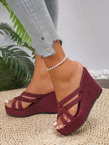 Gros plan de sandales à talons compensés en daim bordeaux élégantes à brides croisées.