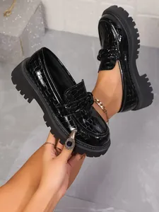 Détail de mocassins en cuir verni noir à motif crocodile et semelles crantées.
