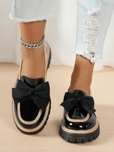 Close-up of stylish black patent leather platform loafers with bows on a model