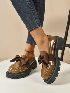 Detail of women's brown patent leather platform loafers with a stylish decorative bow tie