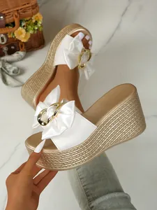 Elegante weiße Schleifensandalen mit Goldschnalle und strohgewebter Keilsohlendetail
