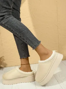 Vista detallada de elegantes zuecos de nieve beige con plataforma y vaqueros grises