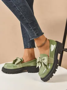 Close-up detail of stylish green bow loafers featuring chunky black platform soles and glossy finish