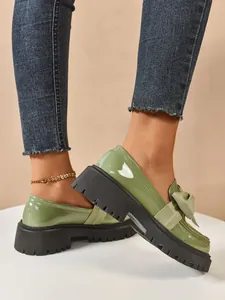 Close-up showing the glossy green patent leather and bow detail on platform loafers