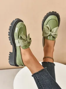 Close-up detail of stylish green patent leather platform loafers with oversized satin bows