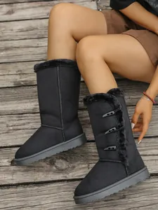 Detail shot of black faux fur lined snow boots with horn buckles on wooden floor.