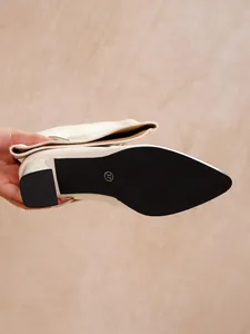 Detail view of the black non-slip sole and chunky heel of a cream pointed toe boot.