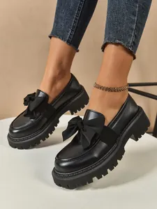 Close-up of black platform loafers with elegant bow detailing on female model