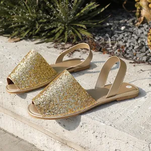 Detail view of sparkling gold glitter flat sandals on a stone surface