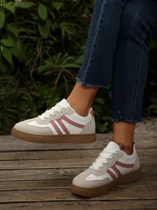 Retro dames sneakers met roze strepen en bruine rubberen zool gedragen aan de voeten.