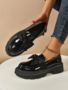 Close-up showing the glossy finish and large bow detail on black platform loafers
