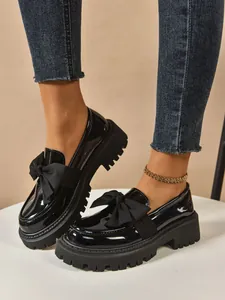 Close-up of black patent leather platform loafers with decorative bow tie.