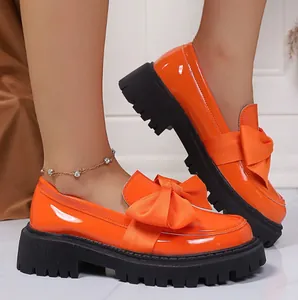 Close-up of vibrant orange patent leather bow loafers with thick black lug soles