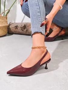 Detailopname van bordeauxrode puntige slingback-hakken met een modieus gouden enkelbandje erbij.