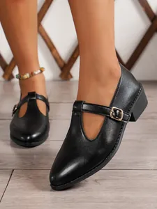 Detailed view of black pointed-toe Mary Jane flats featuring a T-strap and gold buckle.