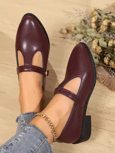 Close-up of burgundy leather T-strap loafers with chunky heels and gold buckle detail.