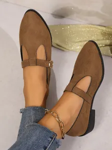 Close-up of brown suede Mary Jane loafers with an elegant buckle strap, worn with jeans.