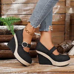 Close-up of black denim wedge shoes featuring straw-braided platform and buckle strap.