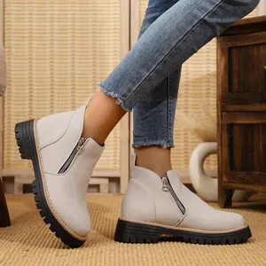 Detail of beige suede ankle boots with stylish side zipper and rugged black lug sole.
