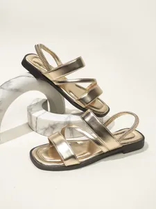 Detailansicht goldener flacher Sandalen mit elastischen Riemen und schwarzer Sohle