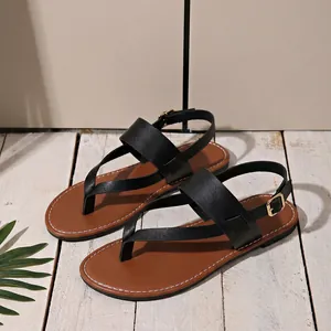 Close-up of black strappy flat sandals with brown footbed on white wood.